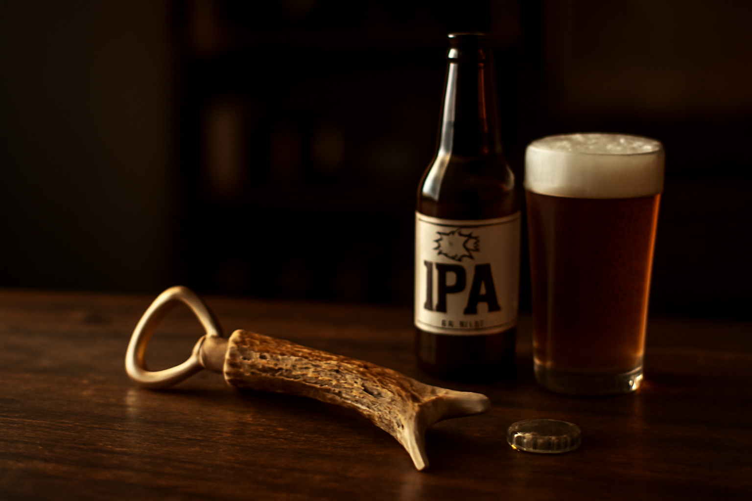 A handcrafted bottle opener with a unique red deer antler handle resting on a dark slate surface next to a full craft beer glass.